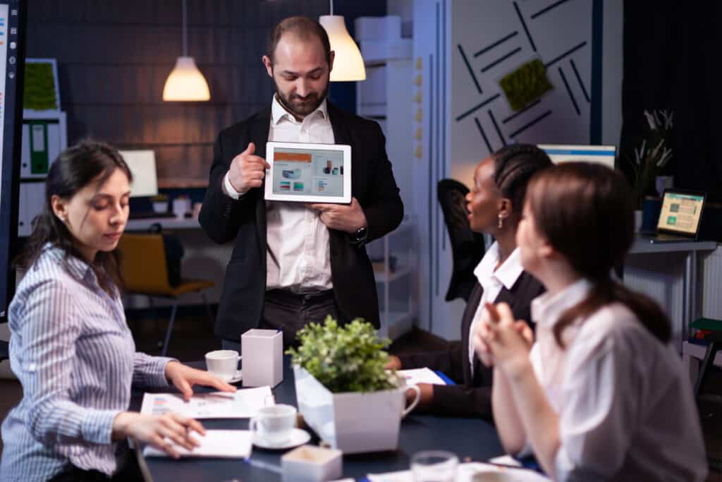 Focused businessman showing corporate graphs presentation using tablet working at company ideas. Diverse multi-ethnic businesspeople brainstorming strategy of wordpress website management in office meeting room